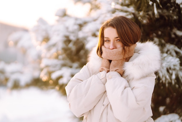 Mulher bonita em um parque nevado. Jovem caminhando em um dia ensolarado de inverno