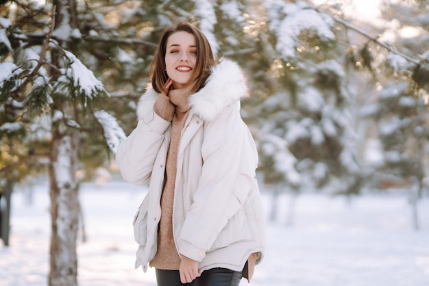 Mulher bonita em um parque nevado. Jovem caminhando em um dia ensolarado de inverno