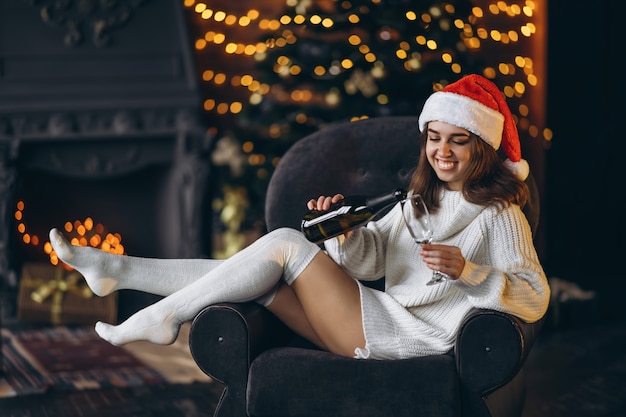 Mulher bonita em um suéter quente, meias e chapéu de Natal, sentada na cadeira com champanhe