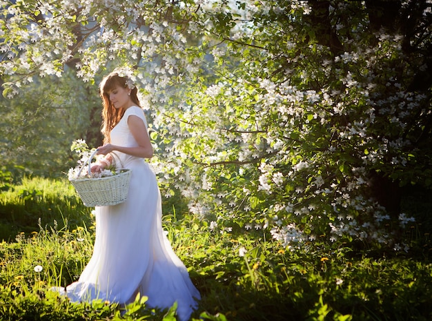 Mulher bonita em um vestido branco no jardim de macieiras de flor. Conceito de conto de fadas