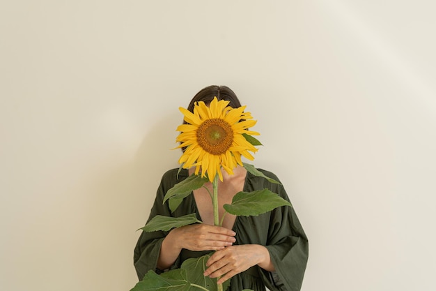 Mulher bonita em vestido de noite verde segura girassol em fundo bege neutro Composição floral de moda estética mínima