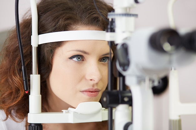 Mulher bonita está olhando para a máquina de teste do olho com concentração no laboratório de oculista