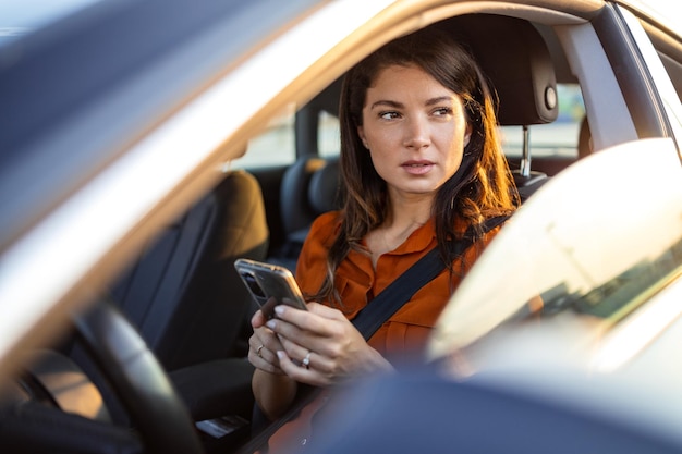Foto mulher bonita está usando um smartphone e sorrindo enquanto está sentada no assento do carro conceito de blog de tecnologia de negócios