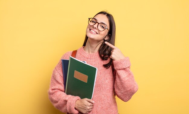 Mulher bonita estudante sorrindo com confiança apontando para o próprio sorriso largo