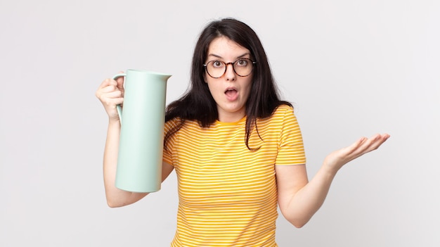 Mulher bonita, extremamente chocada e surpresa, segurando uma garrafa térmica de café