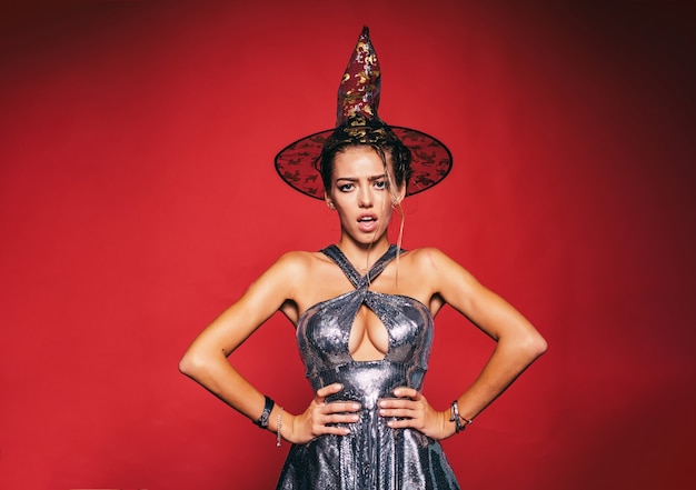 Foto mulher bonita fantasiada de bruxa na festa de halloween. mulher surpresa com rosto lindo e penteado retrô e lábios vermelhos em estúdio sobre fundo vermelho.