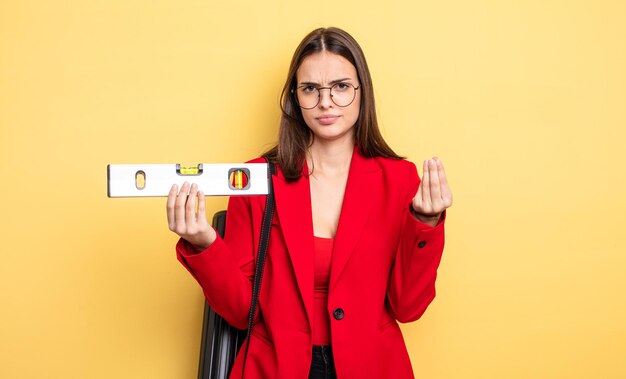 Mulher bonita fazendo gesto capice ou dinheiro, dizendo para você pagar. arquiteto com nível