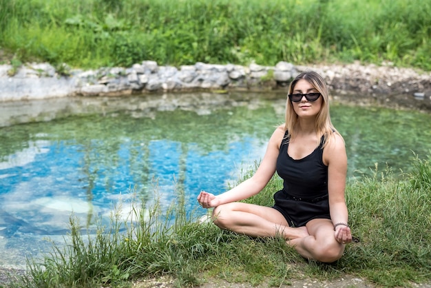 Mulher bonita fazendo ioga perto do lago, ao ar livre