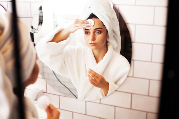 Mulher bonita fazendo procedimentos cosméticos para cuidar da pele do rosto no banheiro