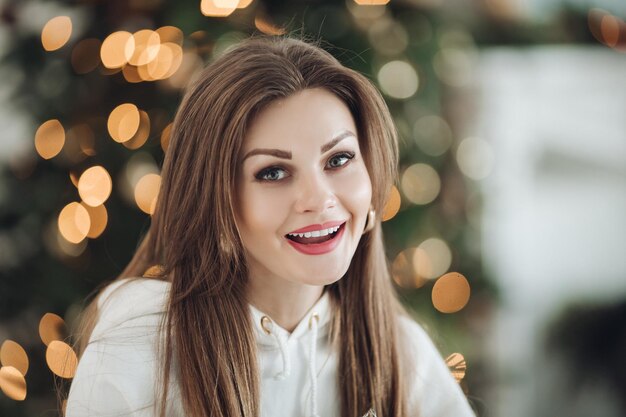 Mulher bonita feliz em um terno branco posando perto da árvore de Natal