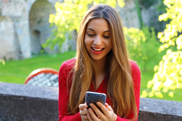 Mulher bonita feliz usando app para smartphone ao ar livre