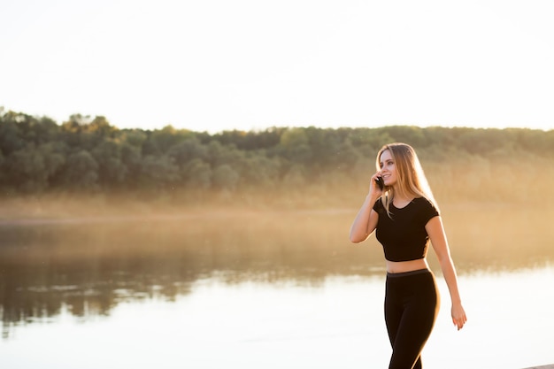 Mulher bonita fitness em um top preto e legging falando em um smartphone e sorrisos.