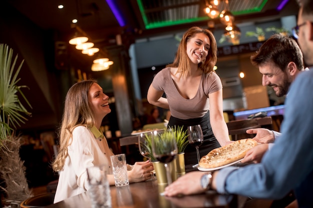 Mulher bonita garçom servindo grupo de amigos com comida no restaurante