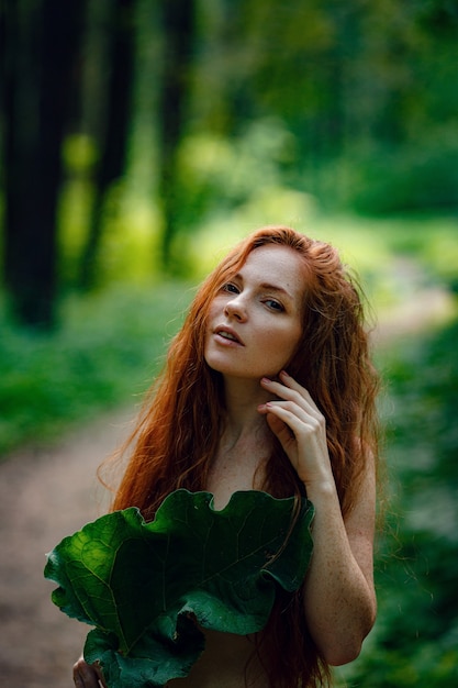 Mulher bonita gengibre segurando uma grande licença sobre o peito sem roupas em uma floresta