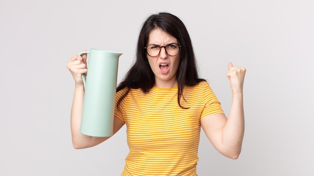 Mulher bonita gritando agressivamente com uma expressão de raiva e segurando uma garrafa térmica de café