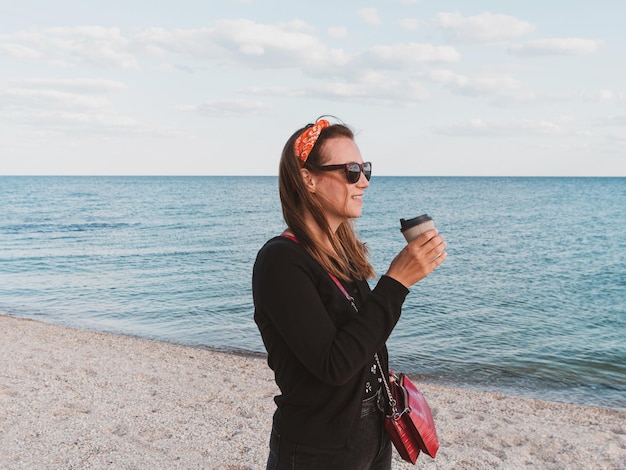 Mulher bonita hipster em cabelo comprido bandana andando no fundo do mar com foto de viagem da vida real de estilo de vida de xícara de café