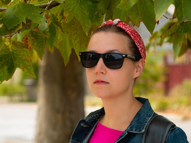 Mulher bonita hipster em óculos de sol camisa rosa bandana vermelha e jaqueta jeans no fundo da natureza em dia ensolarado de outono