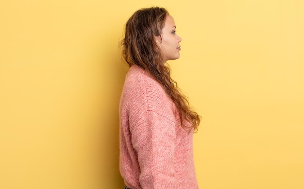 Mulher bonita hispânica em vista de perfil olhando para copiar o espaço à frente, pensando, imaginando ou sonhando acordada