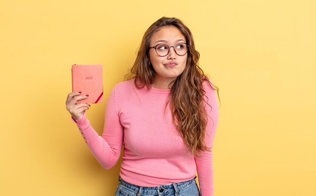 Mulher bonita hispânica encolhendo os ombros sentindo-se confuso e incerto conceito de agenda