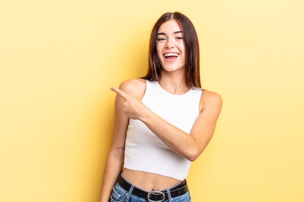 Mulher bonita hispânica parecendo animada e surpresa apontando para o lado e para cima para copiar o espaço