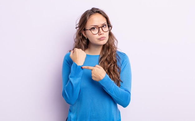 Mulher bonita hispânica parecendo impaciente e com raiva, apontando para o relógio, pedindo pontualidade, quer chegar na hora