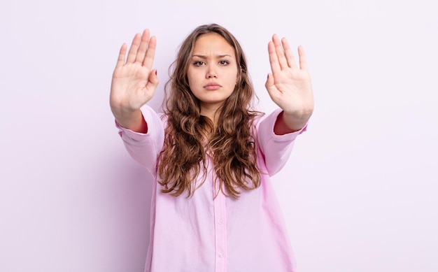 Mulher bonita hispânica parecendo séria, infeliz, irritada e descontente, proibindo a entrada ou dizendo pare com as duas palmas abertas