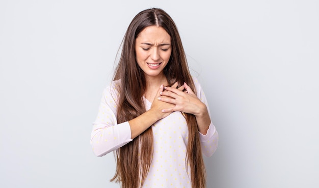 Mulher bonita hispânica parecendo triste, magoada e com o coração partido, segurando as duas mãos perto do coração, chorando e se sentindo deprimida