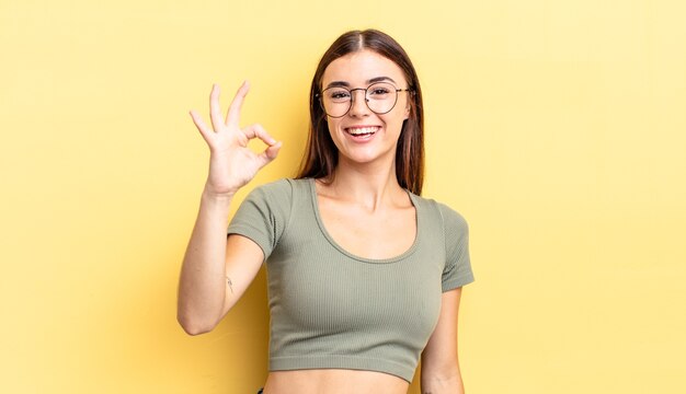 Mulher bonita hispânica se sentindo bem-sucedida e satisfeita, sorrindo com a boca bem aberta, fazendo sinal de ok com a mão