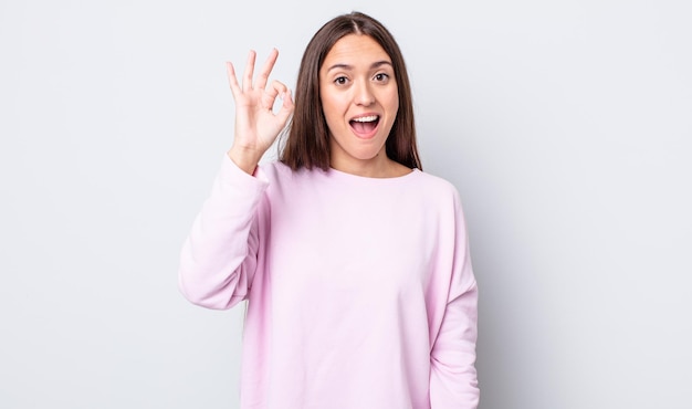 Mulher bonita hispânica se sentindo bem-sucedida e satisfeita, sorrindo com a boca bem aberta, fazendo sinal de ok com a mão