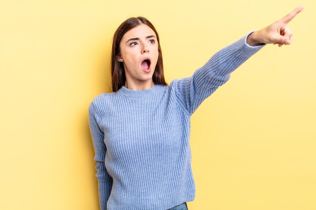 Mulher bonita hispânica se sentindo chocada e surpresa, apontando e olhando para cima com admiração e expressão boquiaberta