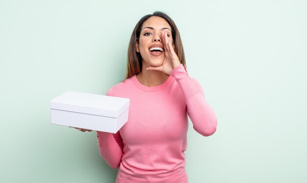 Mulher bonita hispânica se sentindo feliz, dando um grande grito com as mãos perto da boca. conceito de embalagem caixa branca