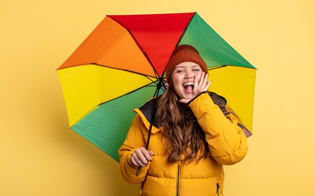 Mulher bonita hispânica se sentindo feliz, dando um grande grito com as mãos perto da boca. conceito de guarda-chuva