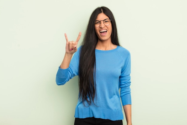 Mulher bonita hispânica se sentindo feliz divertida confiante positiva e rebelde fazendo sinal de rock ou heavy metal com a mão