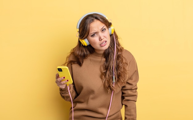 Mulher bonita hispânica se sentindo perplexa e confusa. conceito de fones de ouvido e smartphone