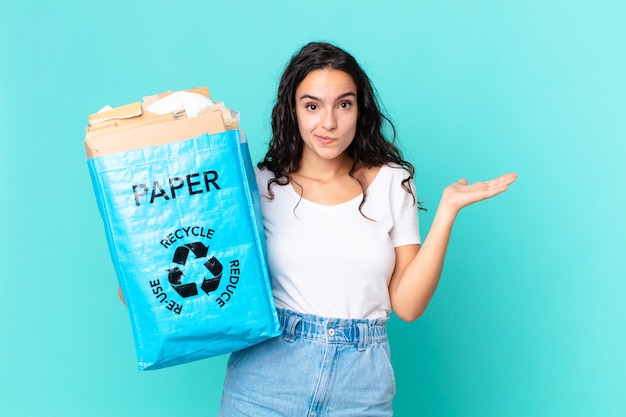 Mulher bonita hispânica se sentindo perplexa e confusa, duvidando e segurando um saco de papel reciclado