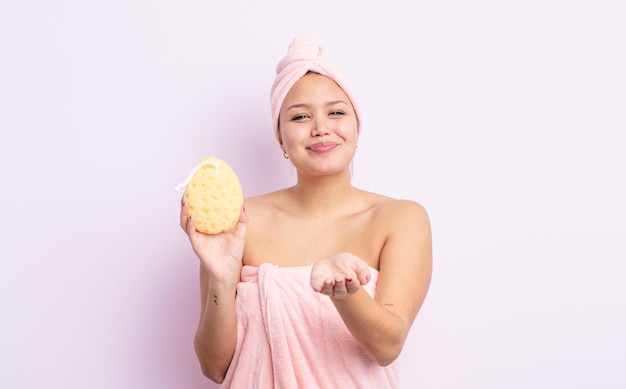 Mulher bonita hispânica sorrindo alegremente com amigável e oferecendo e mostrando um conceito de roupão de banho e esponja