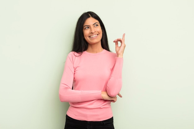 Mulher bonita hispânica sorrindo alegremente e olhando de soslaio pensando ou tendo uma ideia