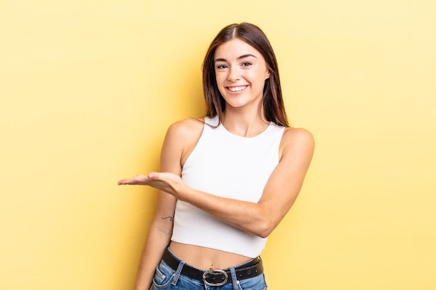 Mulher bonita hispânica sorrindo alegremente, se sentindo feliz e mostrando um conceito no espaço da cópia com a palma da mão