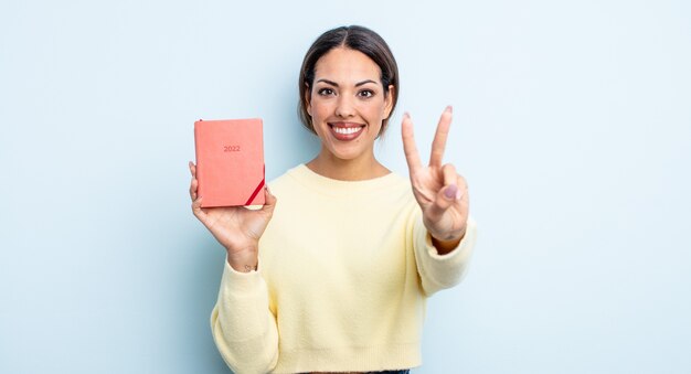 Mulher bonita hispânica sorrindo e parecendo amigável, mostrando o número dois. conceito de agenda