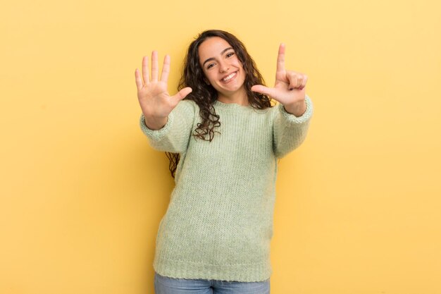 mulher bonita hispânica sorrindo e parecendo amigável, mostrando o número sete ou sétimo com a mão para a frente, em contagem regressiva