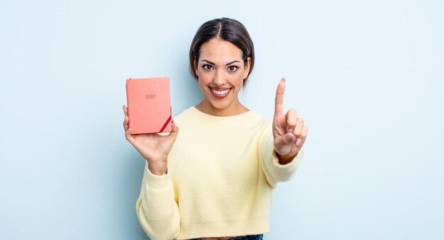 Mulher bonita hispânica sorrindo e parecendo amigável, mostrando o número um. conceito de agenda