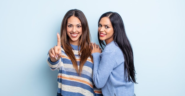 Foto mulher bonita hispânica sorrindo e parecendo amigável, mostrando o número um. conceito de casal de amigos