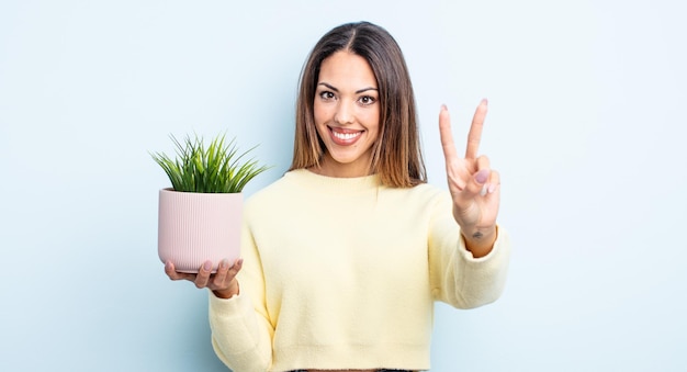 Mulher bonita hispânica sorrindo e parecendo feliz, gesticulando vitória ou paz. conceito de planta de casa