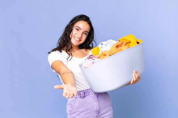 Mulher bonita hispânica sorrindo feliz com simpatia e oferecendo e mostrando um conceito e segurando uma cesta de lavar roupas