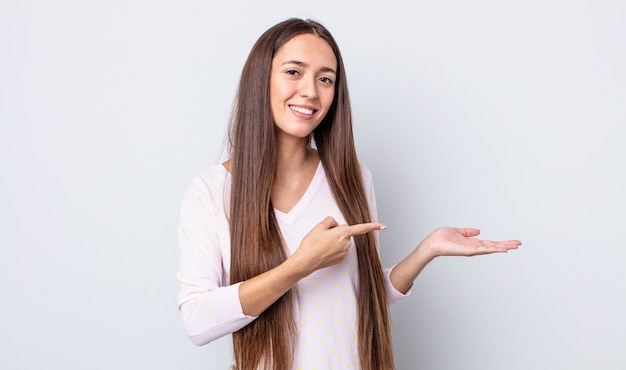 Foto mulher bonita hispânica sorrindo, sentindo-se feliz, despreocupada e satisfeita, apontando para um conceito ou ideia no espaço da cópia ao lado