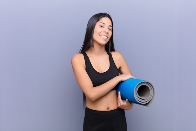 Mulher bonita jovem com um tapete de ioga contra a parede de cimento