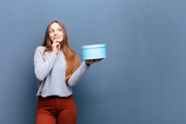 Mulher bonita jovem com uma caixa azul contra a parede azul com um espaço de cópia