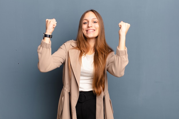 Mulher bonita jovem comemorando um sucesso inacreditável como um vencedor, parecendo animado e feliz dizendo, pegue isso! contra parede cinza