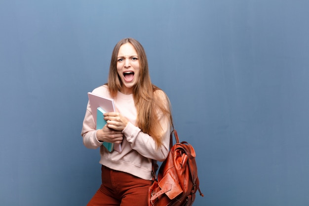 Mulher bonita jovem estudante com livros e bolsa contra a parede azul com um espaço de cópia