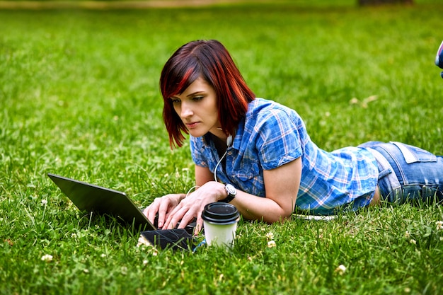 Mulher bonita jovem freelancer usando laptop deitado na grama do parque.